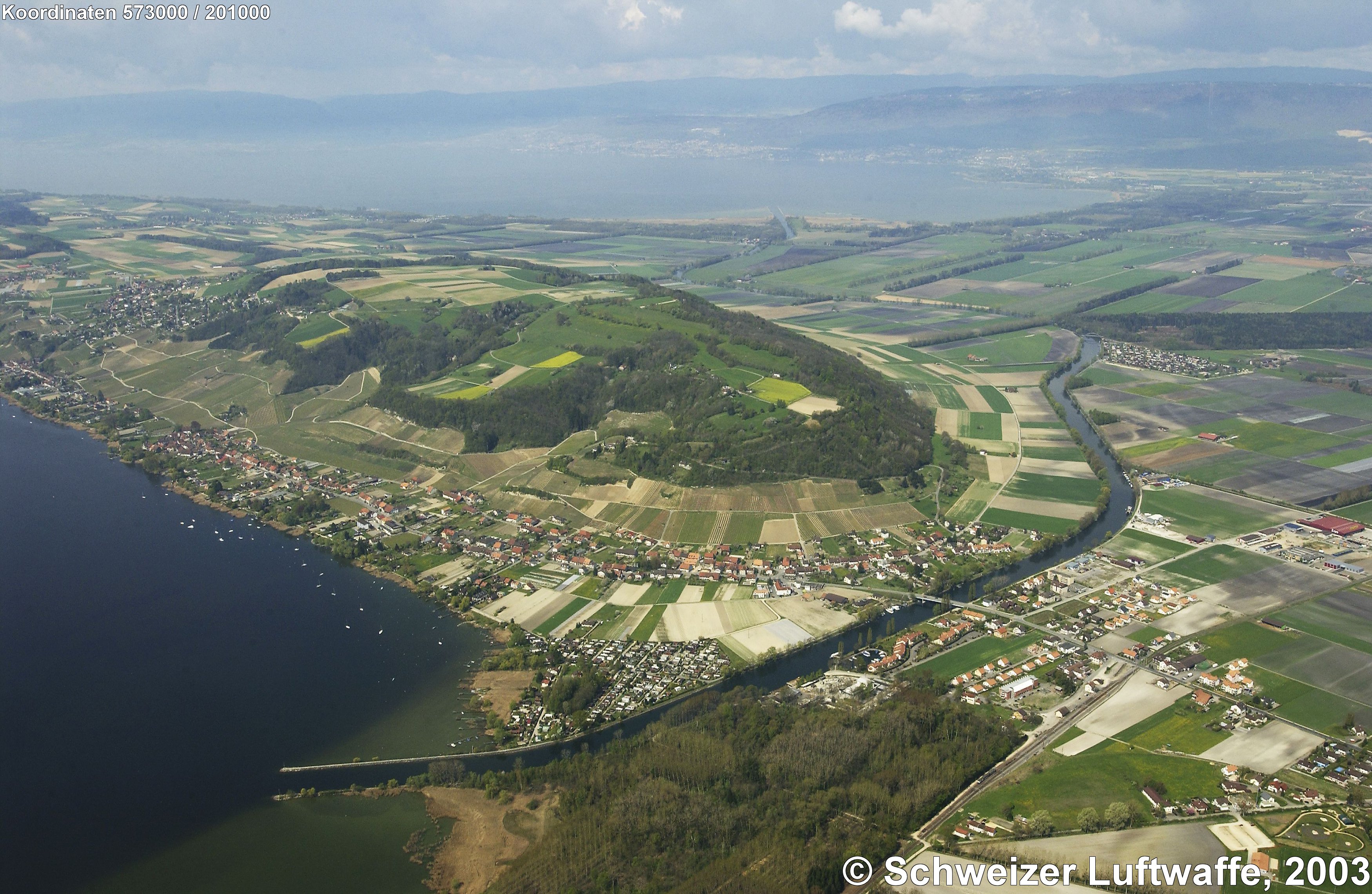 Hügelzug im Zentrum: Mont Vully; davor: Broye-Kanal mit Mündung in den Murtensee; Hintergrund: Neuenburgersee