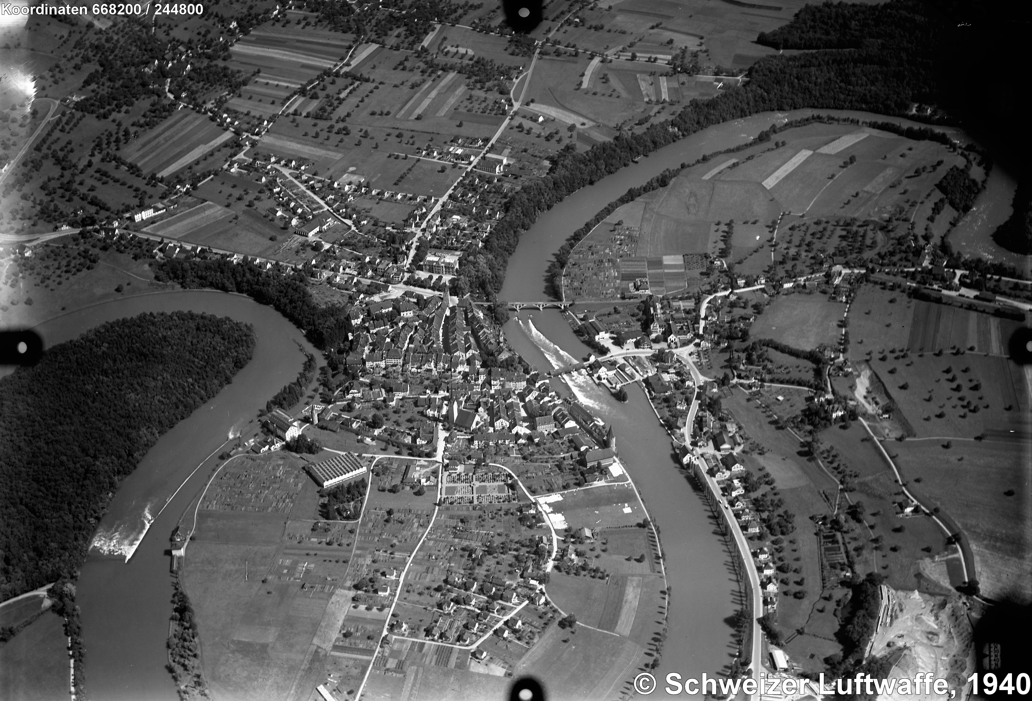 Historische Aufnahme von Bremgarten an der Reuss, anno 1940. Städtchen im Bildzentrum. Brücke oberhalb des Wehrs: Bremgarten-Dietikon-Bahn (BDB; Strecke Dietikon - Wohlen). Brücke Bildmitte: gedeckte Holzbrücke (1281) mit zwei Brückenkapitellen.